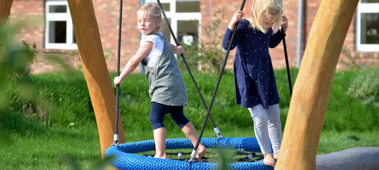 Spielende Kinder auf Spielgerät im Außenbereich der Kita, sonniges Wetter